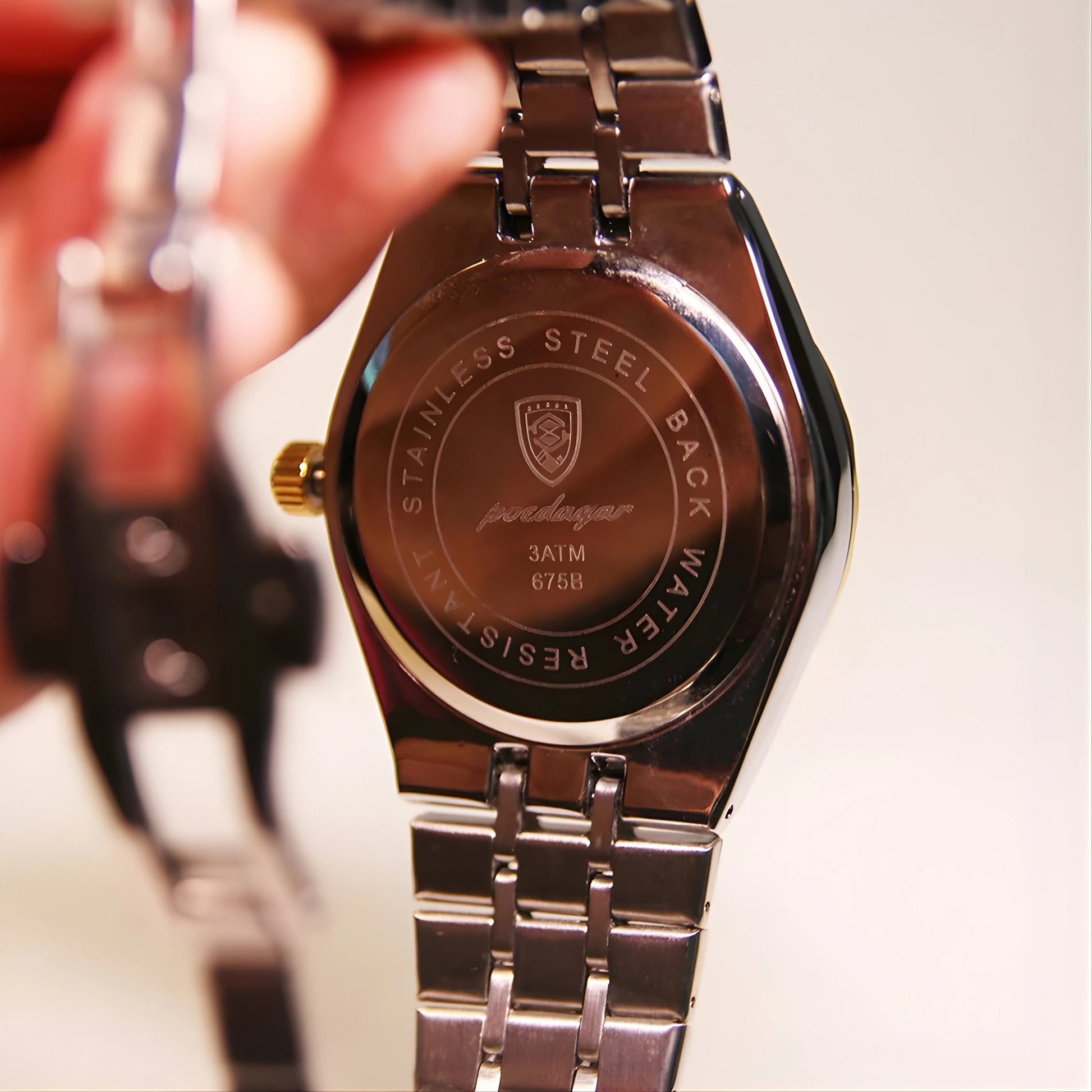 Close-up of a silver watch with brand logo and text on the back, blurred background